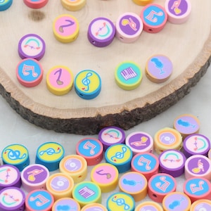 May include: A collection of colorful round beads with various musical symbols and designs, including music notes, records, and a microphone. The beads are made of polymer clay and are perfect for jewelry making or crafting.