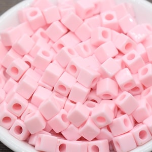 May include: A bowl filled with pink square beads with a hole in the center of each bead.