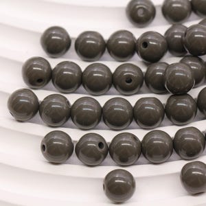May include: A collection of dark brown, glossy, round beads with a hole through the center. The beads are scattered across a white surface, some with visible holes, suggesting they are for stringing or crafting projects.