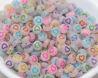 May include: A collection of translucent, pastel-colored beads with heart-shaped designs in various colors. The beads are in a white bowl, showcasing a variety of pink, blue, and purple hues. These beads are ideal for jewelry making and crafts.
