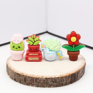 May include: Four small potted plants with cute faces. The plants are a cactus, a succulent, a flower, and a plant with a stack of books. The plants are on a wooden surface.