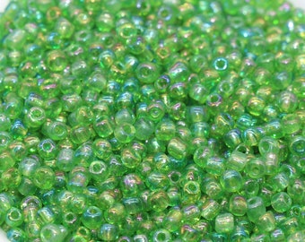 May include: A bowl filled with small, iridescent green glass beads. The beads have a slightly rounded shape and a smooth, shiny finish.