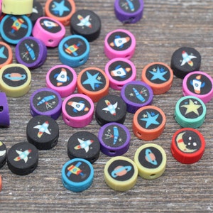 May include: Assortment of colorful round beads with space-themed designs, including rockets, stars, planets, and telescopes. The beads are made of polymer clay and have a hole for stringing.