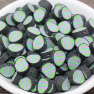 May include: A bowl filled with black and green Easter egg-shaped beads with pink and yellow stripes.