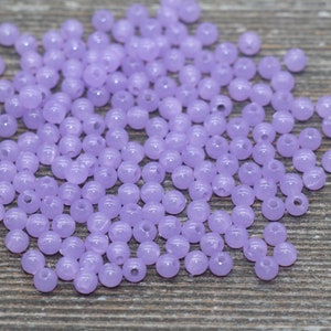 May include: A pile of small, round, lavender-colored beads. The beads are translucent and have a hole in the center.