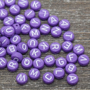 May include: Purple alphabet letter beads with white lettering. The beads are scattered on a wooden surface.