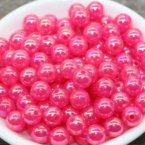 May include: A bowl filled with iridescent pink round beads. The beads have a shiny, pearlescent finish.