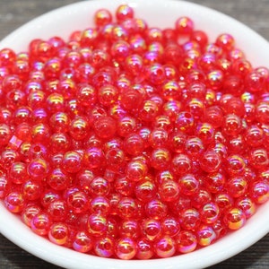 May include: A bowl filled with red iridescent round beads. The beads have a shiny, reflective surface.