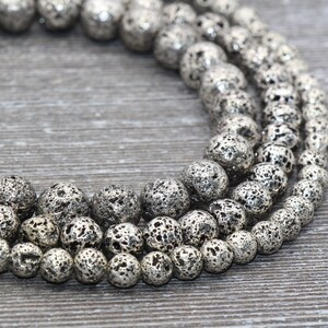 May include: A strand of silver lava rock beads. The beads are round and have a rough, textured surface. The beads are strung on a clear string.
