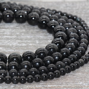 May include: A strand of black onyx beads in various sizes, arranged in a circle on a wooden surface.