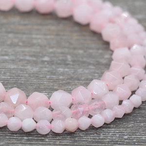 May include: A strand of pink rose quartz beads with faceted, geometric shapes. The beads are strung on a clear elastic cord.