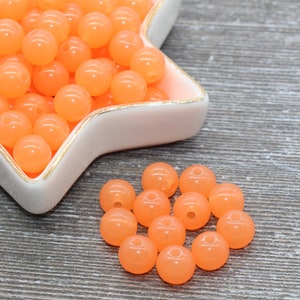 May include: A bowl filled with bright orange beads, with a smaller group of beads scattered on a wood surface.