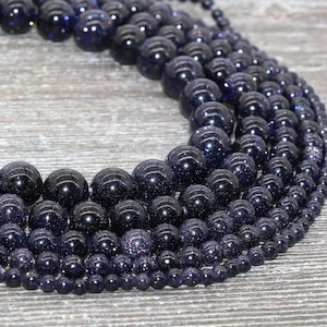May include: A variety of blue star sand beads in different sizes, arranged in a circle on a wooden surface.