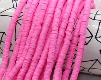 May include: A strand of pink polymer clay beads, each bead is a flat circle, the beads are stacked on top of each other, the beads are on a white background with a black geometric pattern.