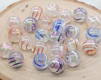 May include: A collection of iridescent glass beads with colorful painted stripes. The beads are round and have a clear glass base with a rainbow iridescent sheen. The stripes are painted in various colors, including blue, orange, and purple.