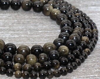 May include: A strand of black and gold gemstone beads. The beads are round and have a smooth, polished finish. The beads are arranged in a circle, with the gold beads on the outside and the black beads on the inside.