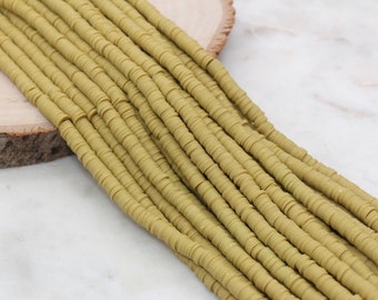 May include: A strand of light green polymer clay beads. The beads are flat and round, and they are arranged in a row. The beads are on a wooden surface.