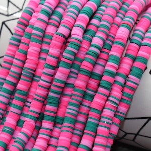 May include: A strand of pink and green polymer clay beads. The beads are flat and round, and they are stacked on top of each other. The beads are arranged in a repeating pattern of pink and green.