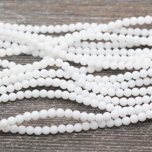 Peut inclure: Un brin de perles rondes blanches, en pierre lisse, opaque et polie. Les perles sont de taille et de forme uniformes et sont enfil&eacute;es sur un fil transparent.