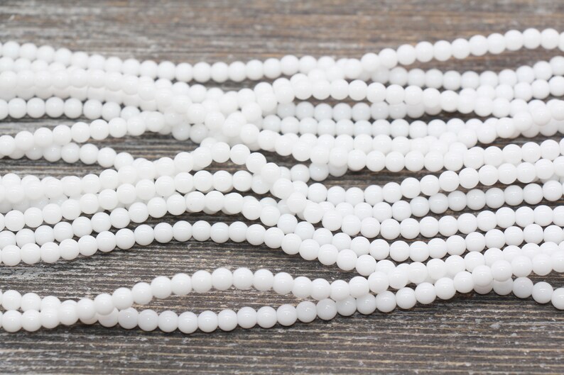 Peut inclure: Un brin de perles rondes blanches, en pierre lisse, opaque et polie. Les perles sont de taille et de forme uniformes et sont enfil&eacute;es sur un fil transparent.