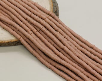 May include: Close-up of strands of light brown, flat, disc-shaped beads. The beads are strung together, creating a textured, linear pattern. The beads are arranged diagonally across a light-colored surface, suggesting a craft or jewelry-making theme.