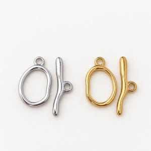 May include: Two toggle clasps for jewelry making, one in a silver tone and one in a gold tone. Each set consists of an irregular, rounded open loop and a matching bar component with a small circular attachment ring on the side of the bar.