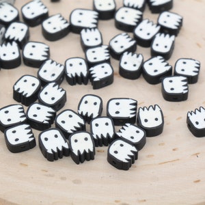 May include: A collection of black and white ghost-shaped beads with a white face and a black outline. The beads are scattered on a wooden surface.