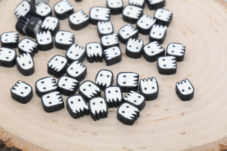 May include: A collection of black and white ghost-shaped beads with a white face and a black outline. The beads are scattered on a wooden surface.