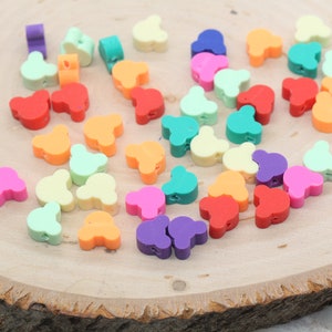 May include: Assortment of colourful plastic bear-shaped beads in various colours, including red, orange, yellow, green, blue, purple, and pink. The beads are arranged on a wooden surface.