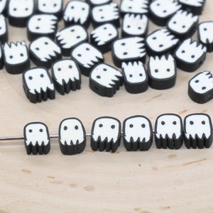 May include: A collection of black and white ghost-shaped beads with a white face and two eyes. The beads are strung on a silver wire.