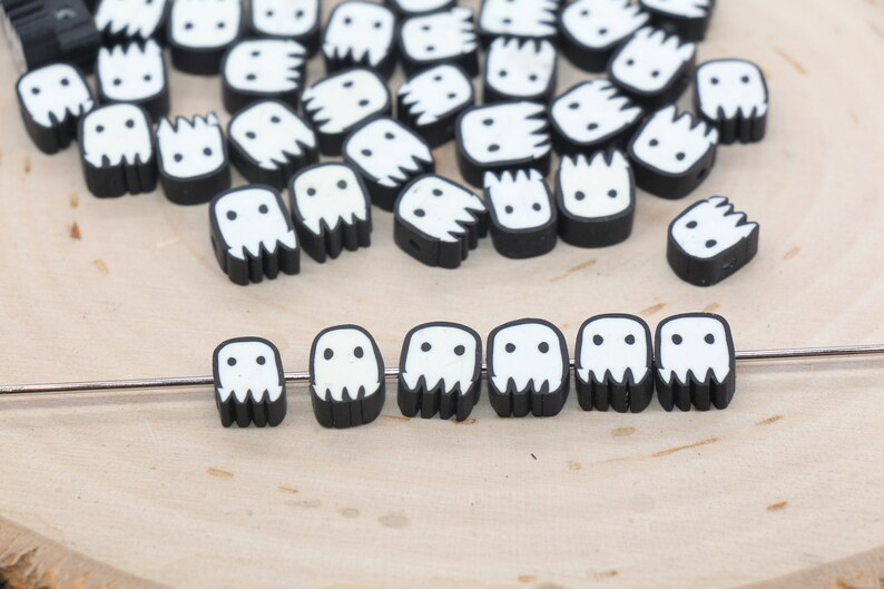 May include: A collection of black and white ghost-shaped beads with a white face and two eyes. The beads are strung on a silver wire.