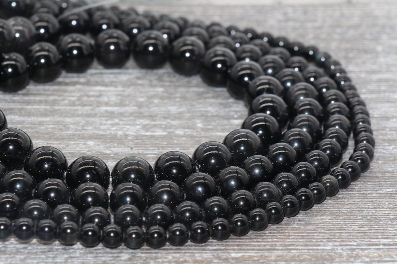 May include: A strand of black onyx beads in various sizes, arranged in a circle on a wooden surface.