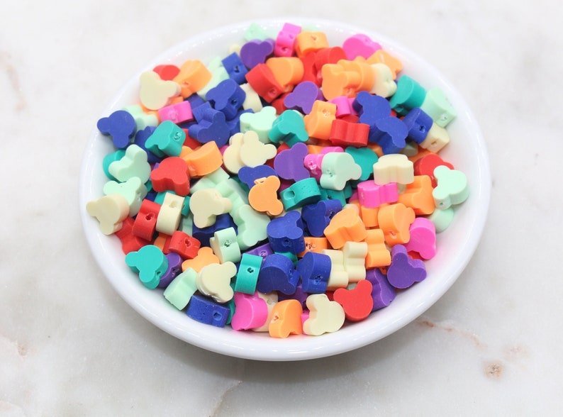 May include: A bowl filled with colourful plastic beads shaped like Mickey Mouse ears. The beads are in various shades of red, orange, yellow, green, blue, and purple.