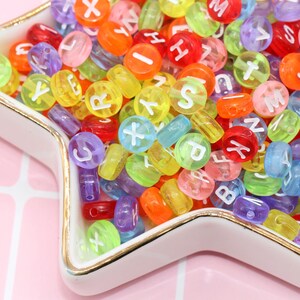 May include: A close-up of a star-shaped dish filled with colourful alphabet beads. The beads are made of translucent plastic and have white letters printed on them.