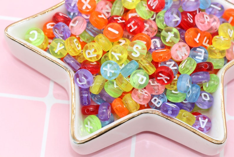 May include: A close-up of a star-shaped dish filled with colourful alphabet beads. The beads are made of translucent plastic and have white letters printed on them.