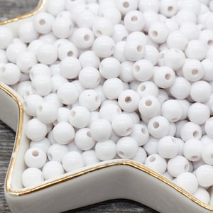 May include: A bowl filled with white round plastic beads. The beads have a hole in the center for stringing.