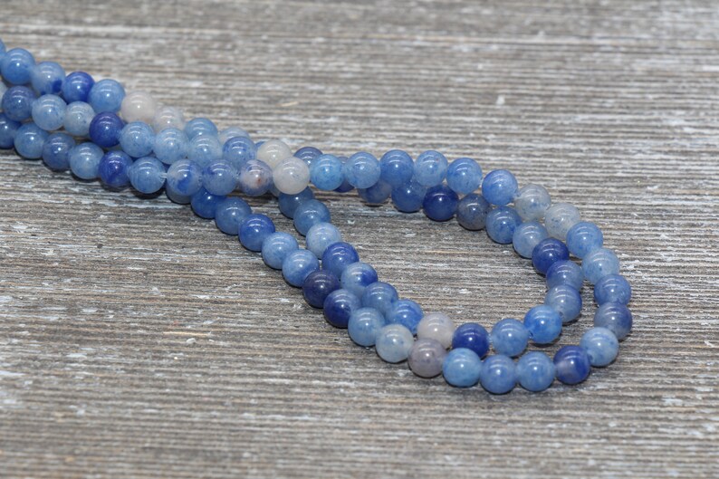 Pode incluir: Close-up de contas de pedras preciosas azuis em tons variados de azul e branco. As contas s&atilde;o redondas e lisas, com um acabamento brilhante. As contas s&atilde;o enfiadas, criando um colar ou uma pulseira.