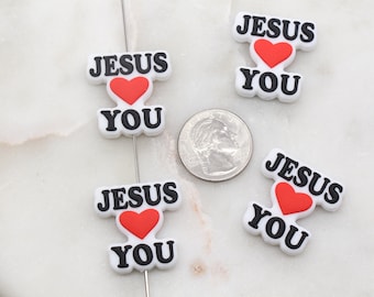 May include: Four white plastic charms with the text "Jesus Loves You" in black lettering and a red heart in the center. The charms are on a white surface.