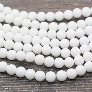 Peut inclure: Un brin de perles rondes blanches, en pierre lisse et polie. Les perles sont de taille et de forme uniformes et ont une finition brillante.