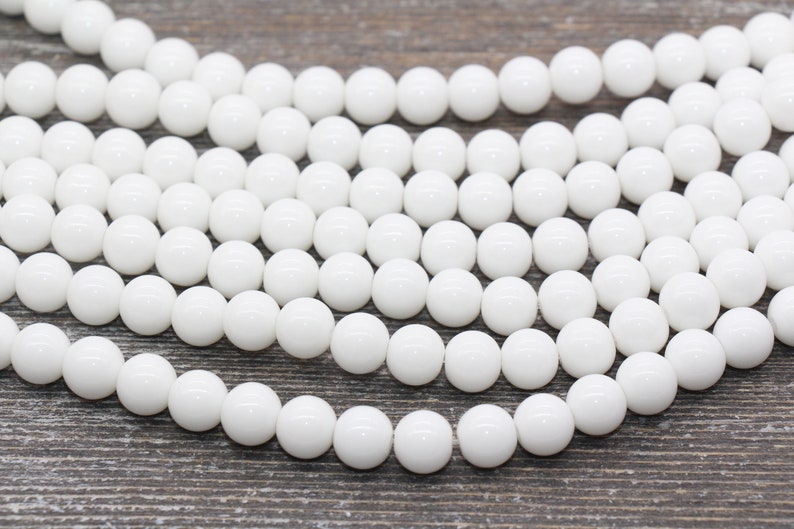 Peut inclure: Un brin de perles rondes blanches, en pierre lisse et polie. Les perles sont de taille et de forme uniformes et ont une finition brillante.