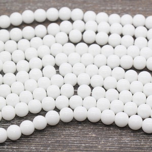 Peut inclure: Un brin de perles rondes blanches, en pierre lisse et polie. Les perles sont de taille et de forme uniformes, et elles sont dispos&eacute;es en un motif l&acirc;che et fluide.