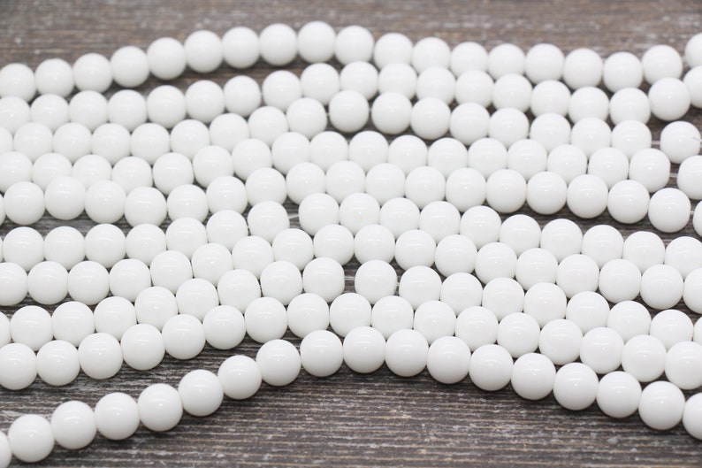 Peut inclure: Un brin de perles rondes blanches, en pierre lisse et polie. Les perles sont de taille et de forme uniformes, et elles sont dispos&eacute;es en un motif l&acirc;che et fluide.
