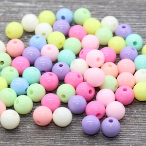 May include: A large pile of pastel colored plastic beads. The beads are round and have a hole in the center. The beads are a variety of colors, including pink, blue, green, yellow, and purple.