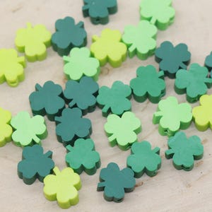 May include: A collection of green and light green wooden shamrock beads. The beads are shaped like four-leaf clovers.
