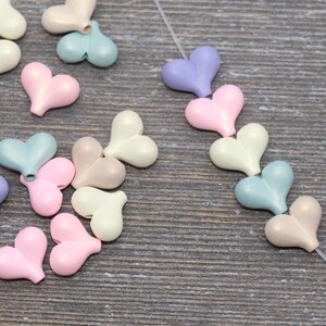 May include: Assortment of pastel colored heart shaped beads. The beads are strung on a clear thread. The beads are in shades of pink, blue, and cream.
