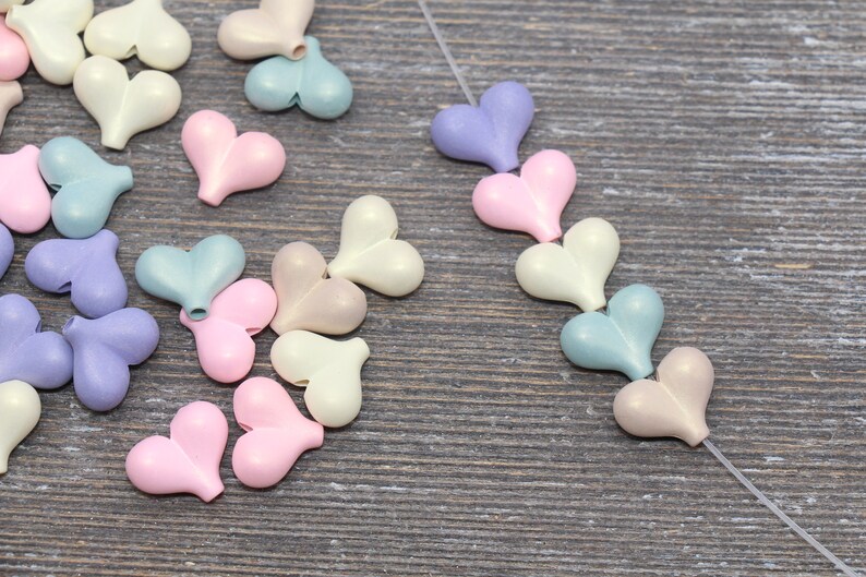 May include: Assortment of pastel colored heart shaped beads. The beads are strung on a clear thread. The beads are in shades of pink, blue, and cream.