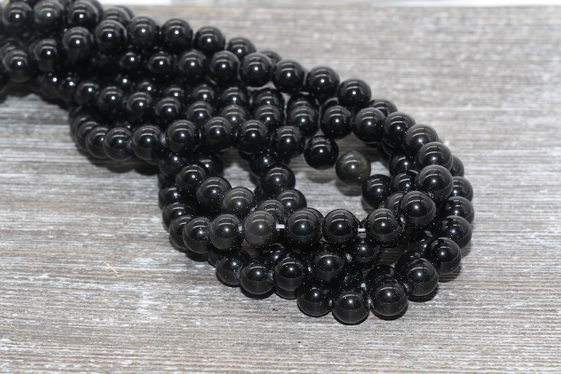 May include: A strand of black gemstone beads, likely obsidian, with a smooth, polished finish. The beads are round and uniform in size, creating a consistent look.