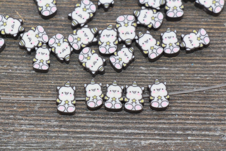May include: A collection of white unicorn-shaped charms with black outlines and gold star accents. The charms are scattered on a wooden surface.