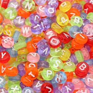 May include: A large assortment of colourful plastic alphabet beads. The beads are translucent and have white letters on them. The beads are in a variety of colours, including red, orange, yellow, green, blue, purple, and pink.