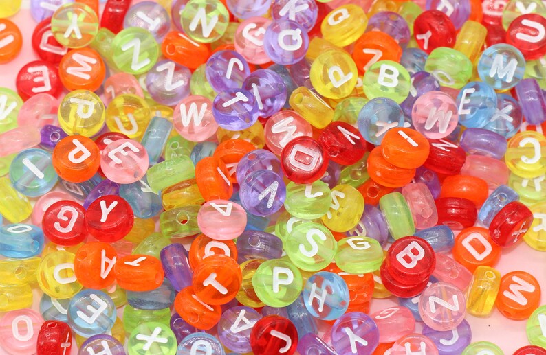 May include: A large assortment of colourful plastic alphabet beads. The beads are translucent and have white letters on them. The beads are in a variety of colours, including red, orange, yellow, green, blue, purple, and pink.